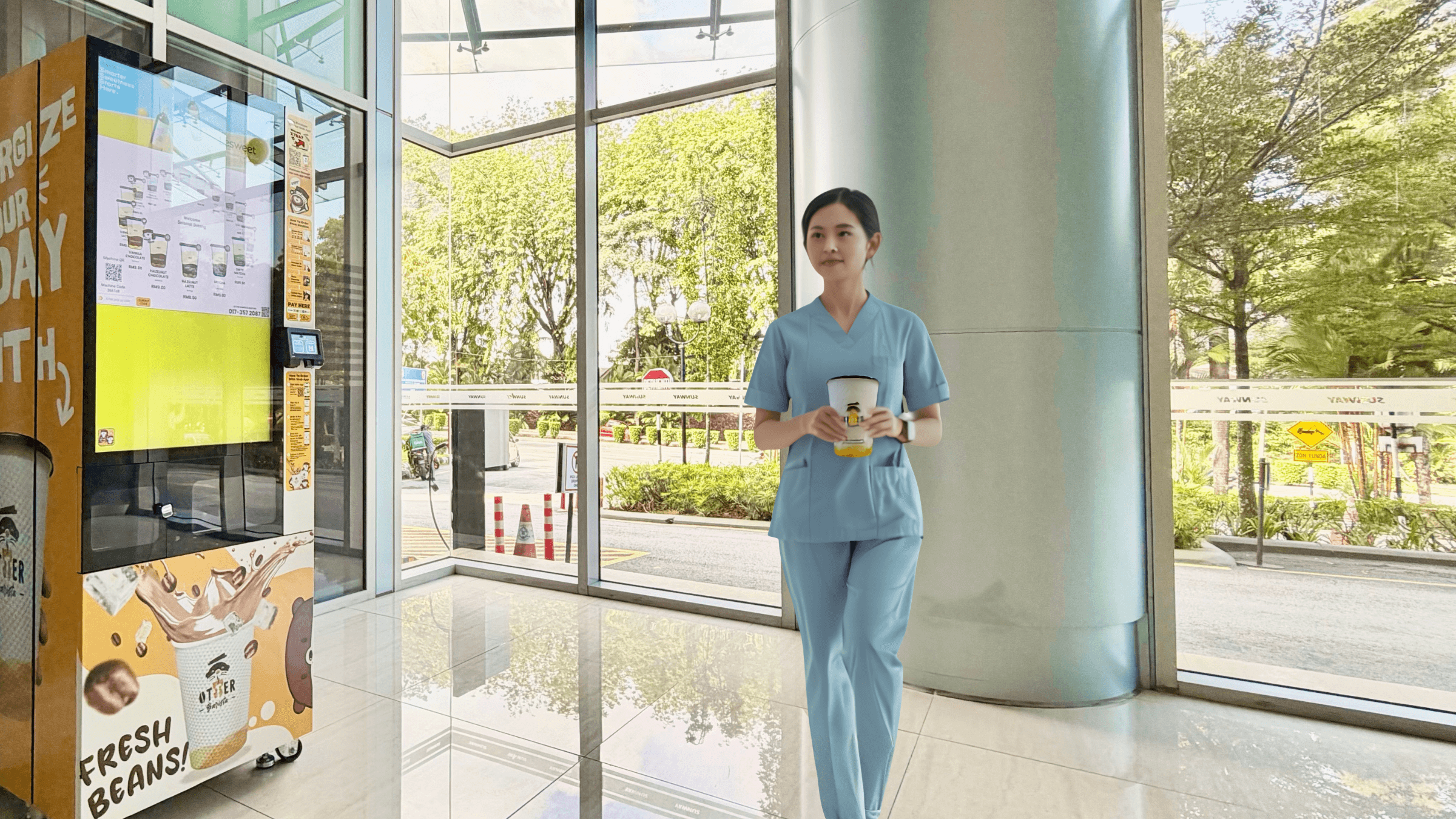 A nurse in scrubs walking through a hospital corridor with a takeaway coffee, past an Otter Barista machine