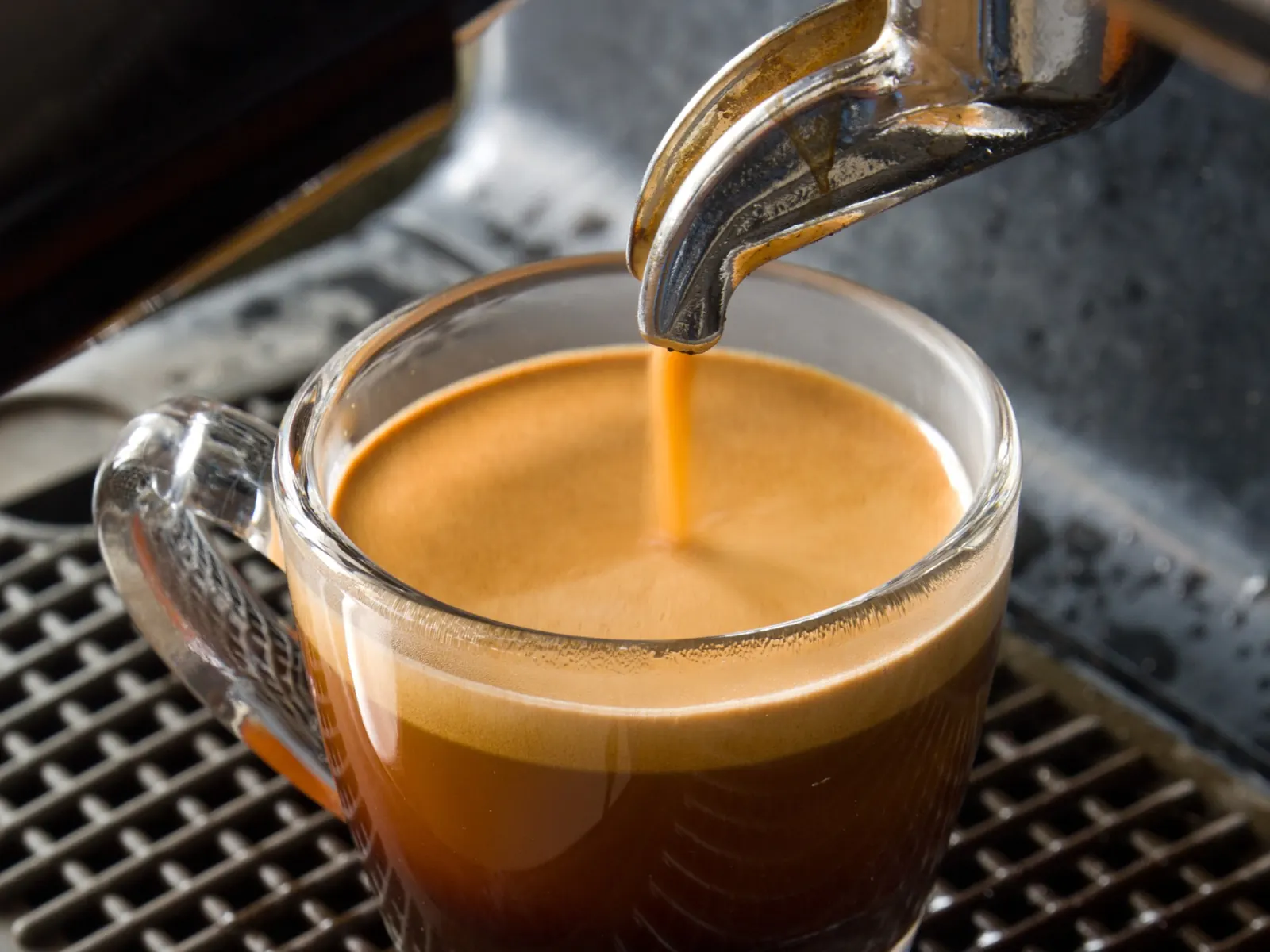 A freshly pulled espresso with crema, beans in the hopper behind